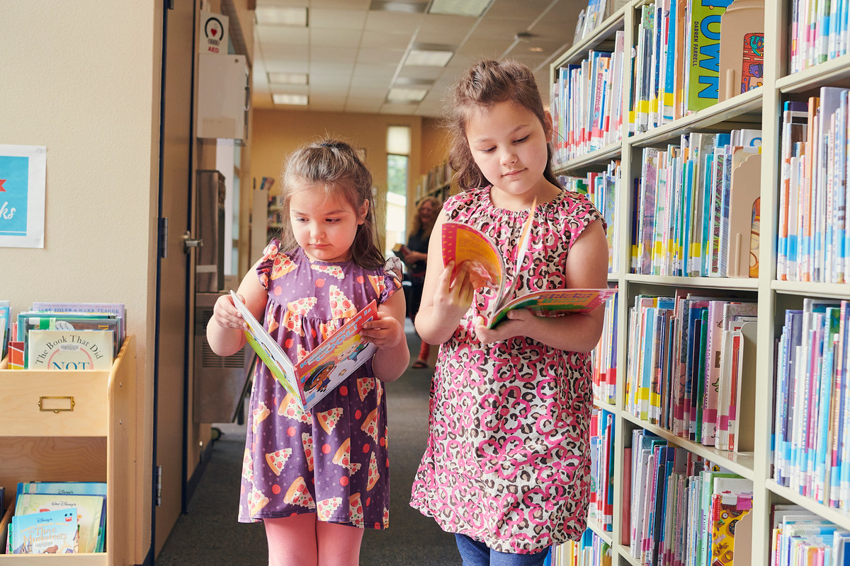 Two girls looking at books next to a bookshelf