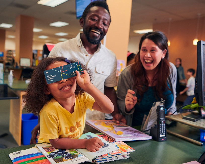 Parents and young daughter smile at the library counter.