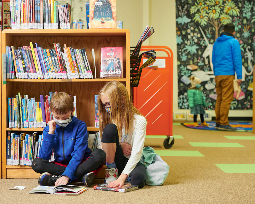 Dos niños leyendo en el suelo de una biblioteca.