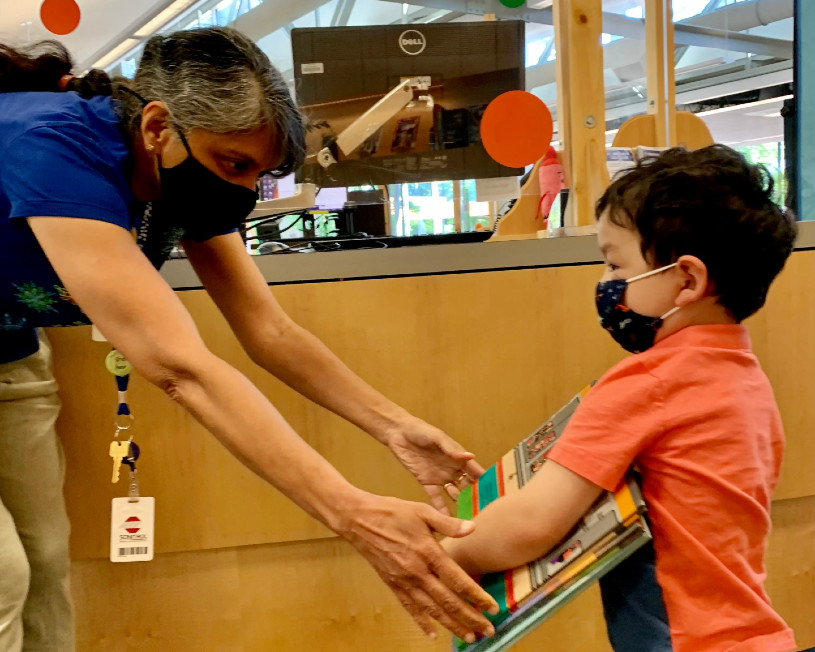 librarian handing books to young boy at service desk