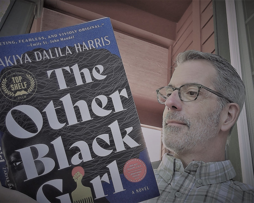 Man with glasses reading The Other Black Girl