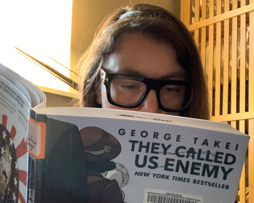 Woman with glasses reads "They Called Us Enemy" by George Takei.