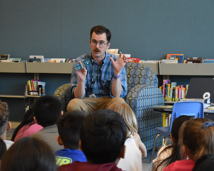 Librarian holds up a library card in front of a class of elementary school students