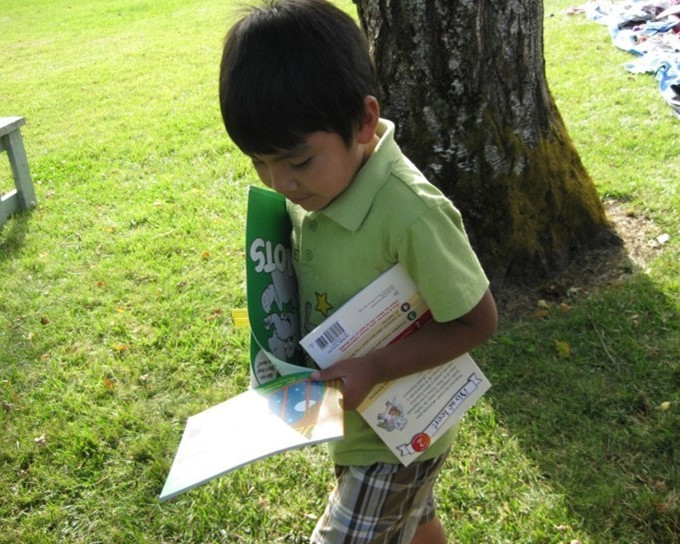 Niño con camisa verde camina por la hierba sosteniendo libros para niños