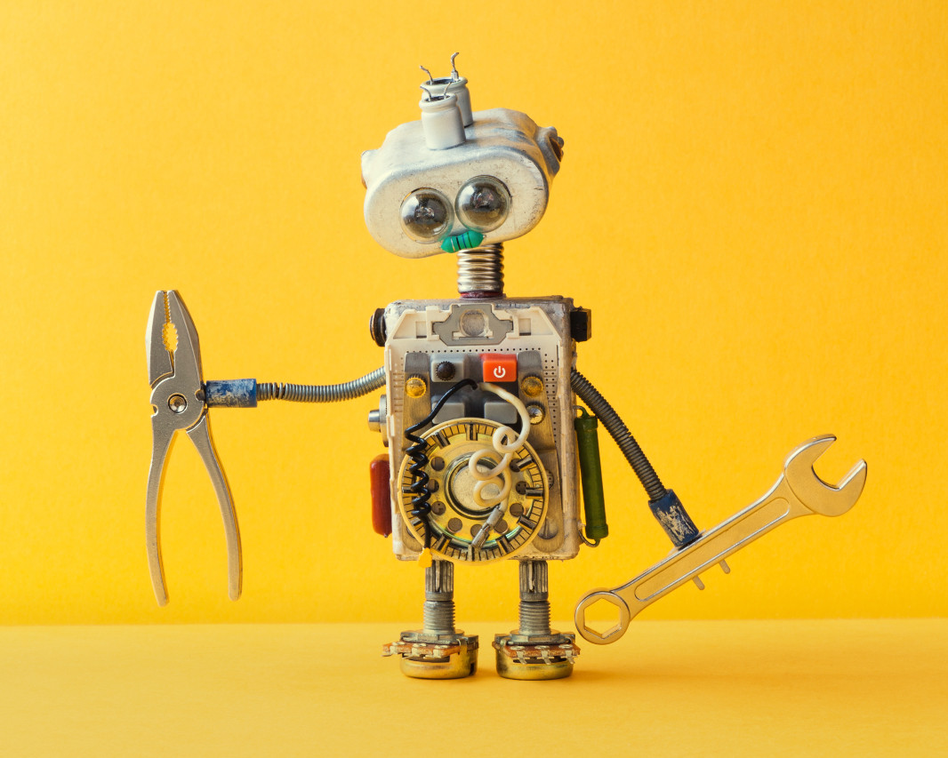Robot holding a wrench and pliers stands on a yellow background