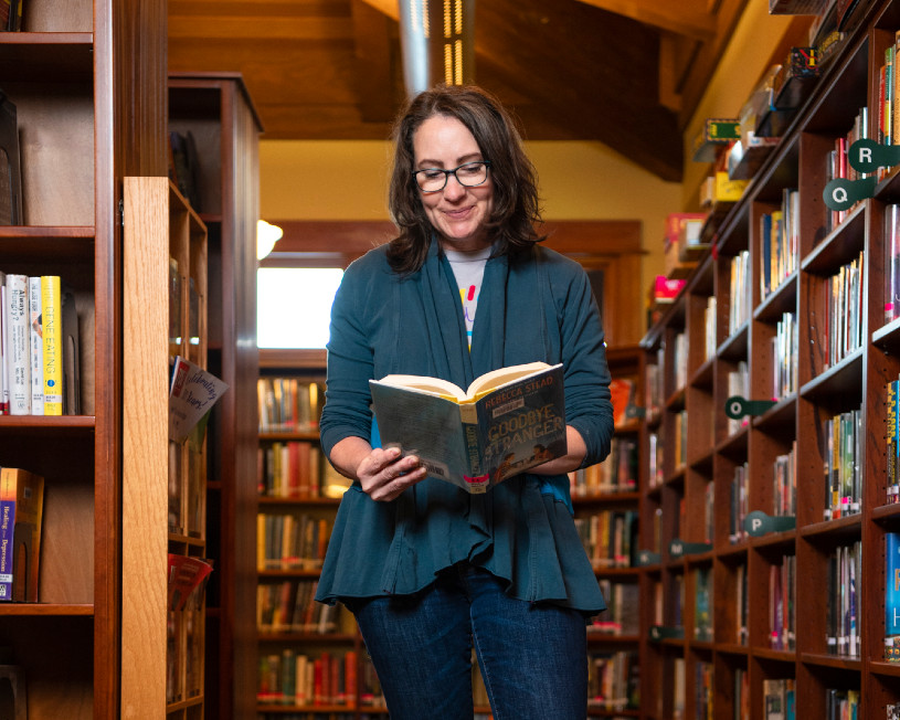 woman standing in a library reading a book