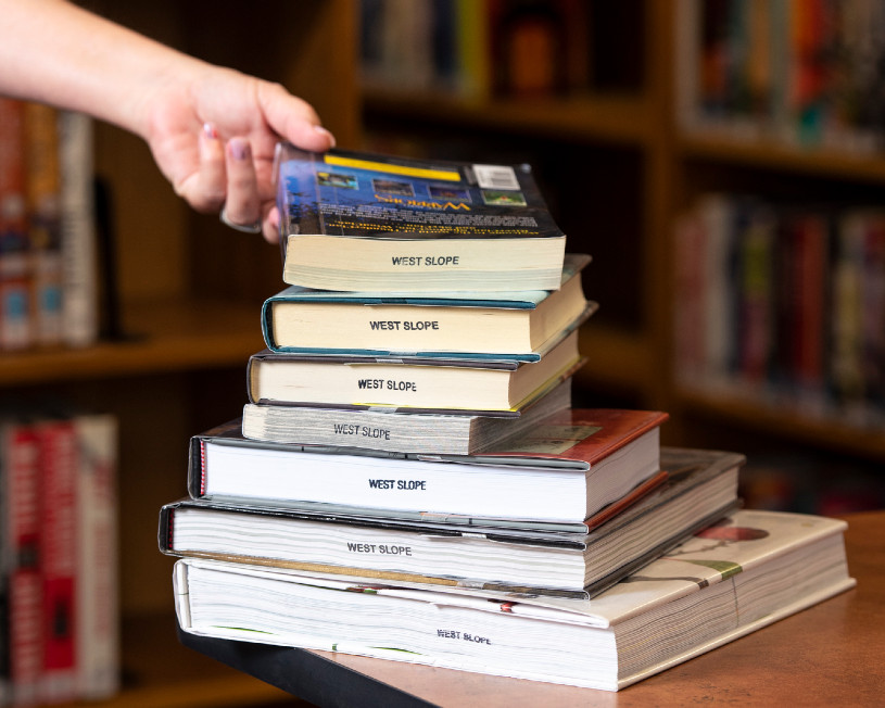 person reaching for a stack of books at a library