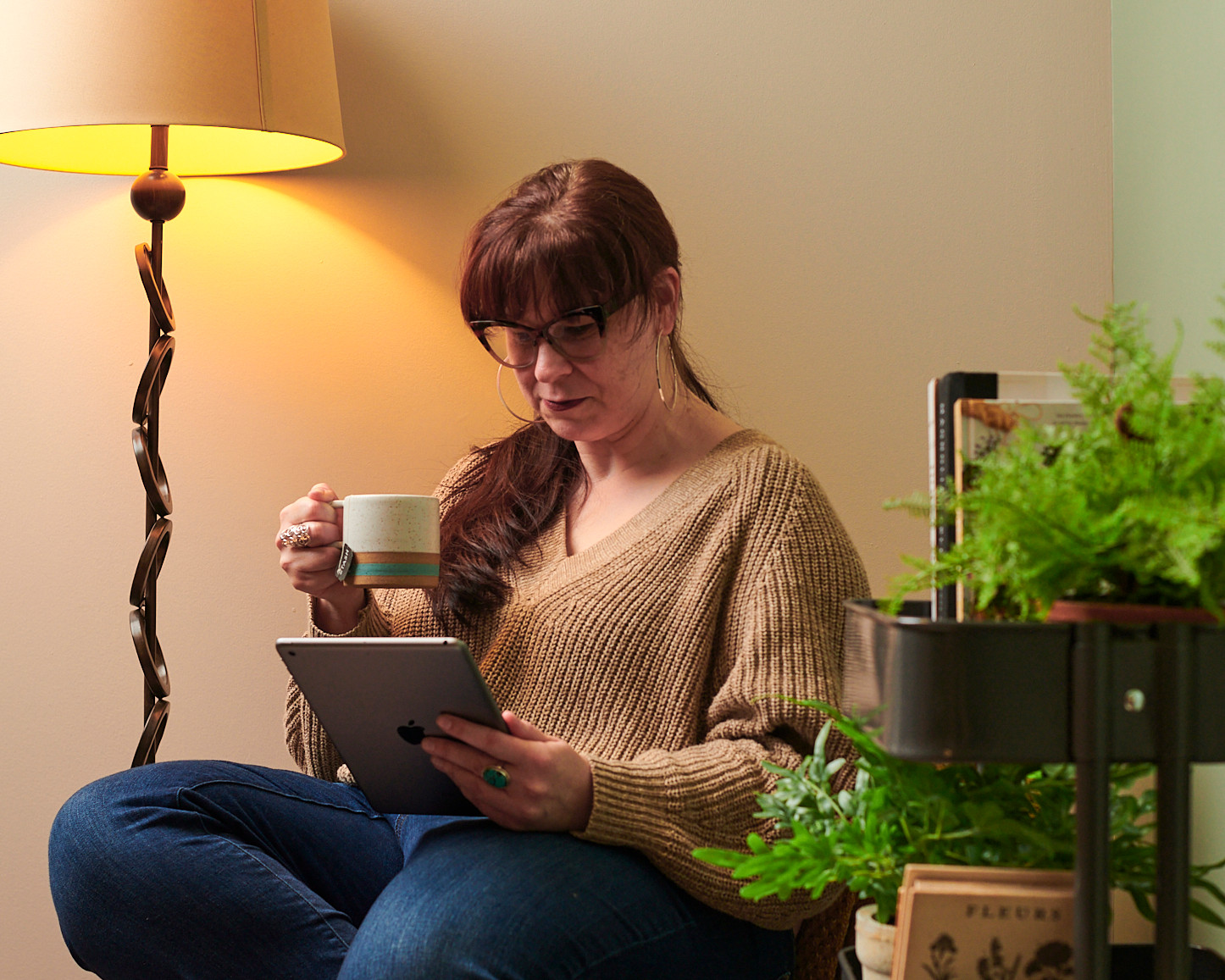 Woman with glasses reading at home on a tablet while drinking tea