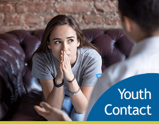 young woman sitting on couch looking at person with their back to the viewer