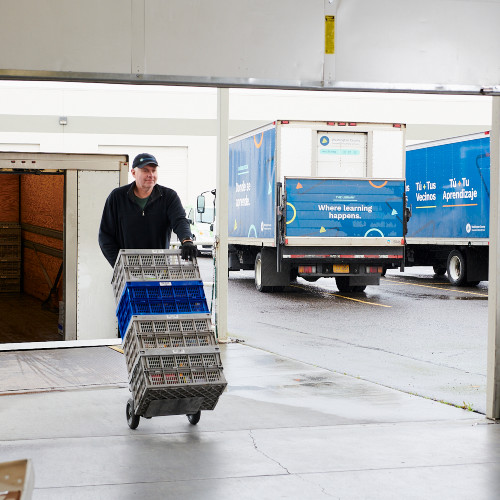 Man pushing dolly of library taskets in warehouse