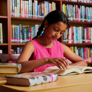 Girl reading a book at a table in front of bookshelves