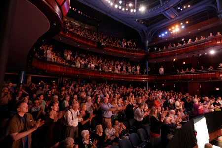Público ovacionando de pie en el interior de un teatro