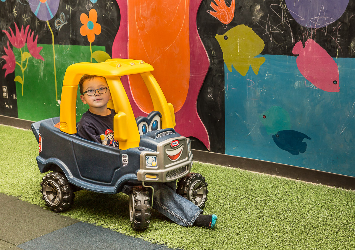 Boy wearing glasses, sitting in toy car