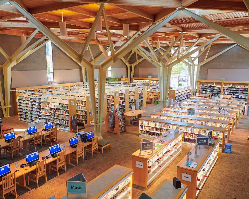 Techo abovedado y vigas vistas dentro de una biblioteca con filas de estantes y computadoras.