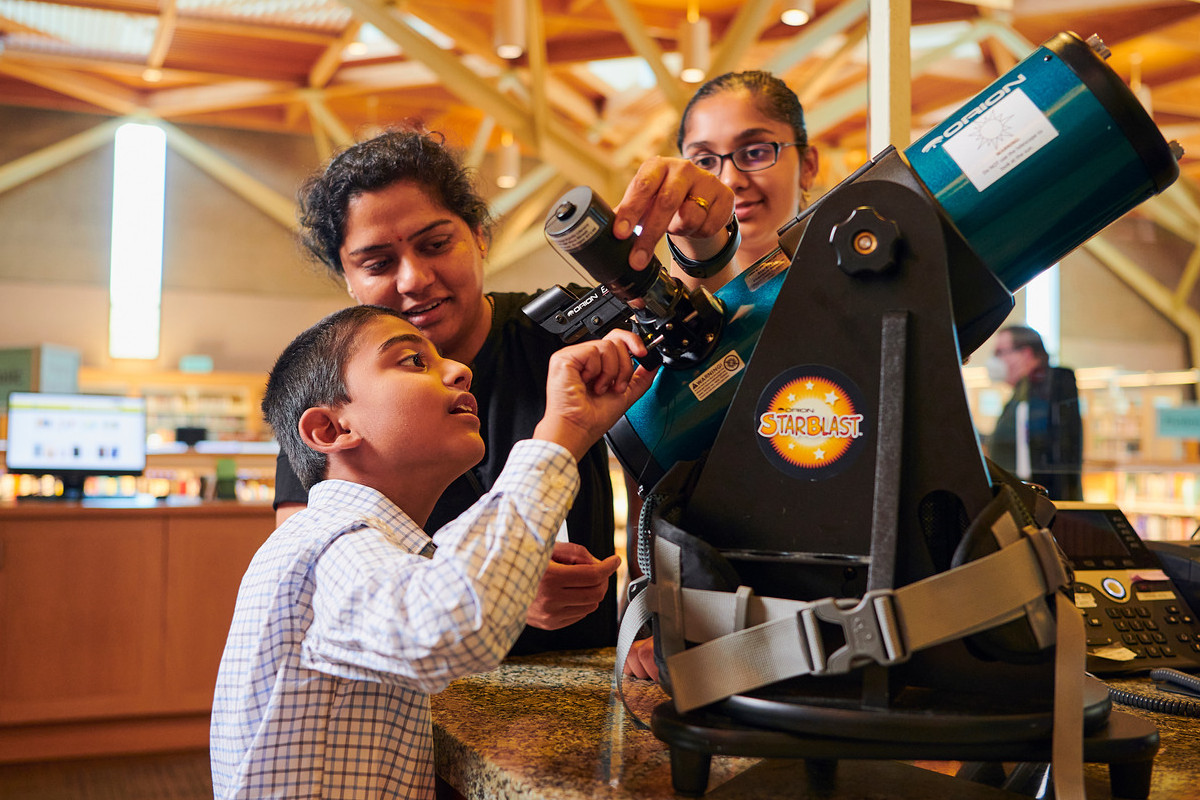 Young boy and two others look at a telescope inside the Sherwood library