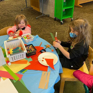 Dos hermanas jóvenes haciendo artes y oficios en una pequeña mesa en la biblioteca