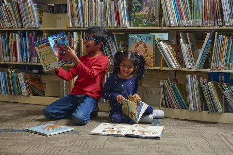 Brother and sister sitting on the floor of the library and reading picture books.