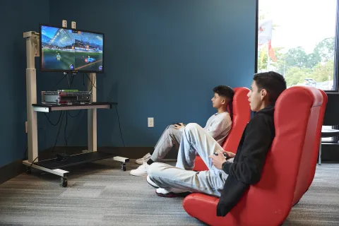 Two teen boys sitting in gaming chairs and looking at a tv while playing a video game.
