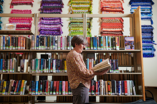 Patron reading book in front of bookshelf and colorful tapestries on wall