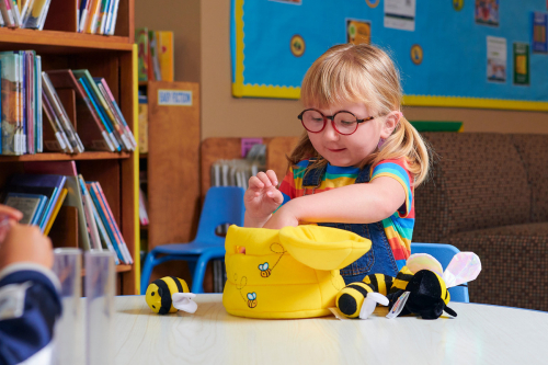 Girl in glasses plays with bee toys at a table