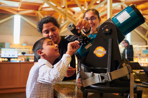 Young boy and two others look at a telescope inside the Sherwood library