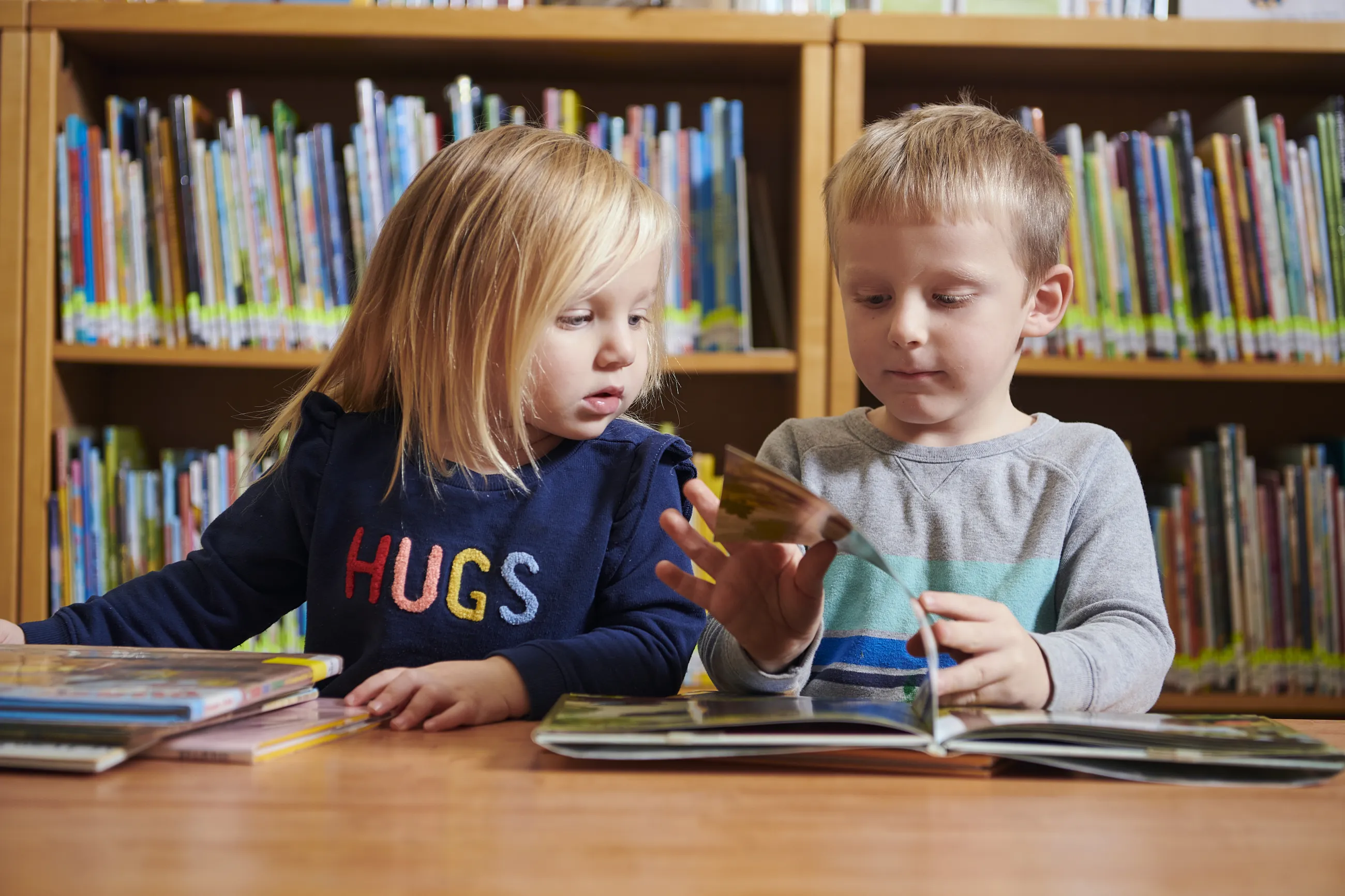 Two toddlers, a girl and a boy, looking at a picture book together in the library.
