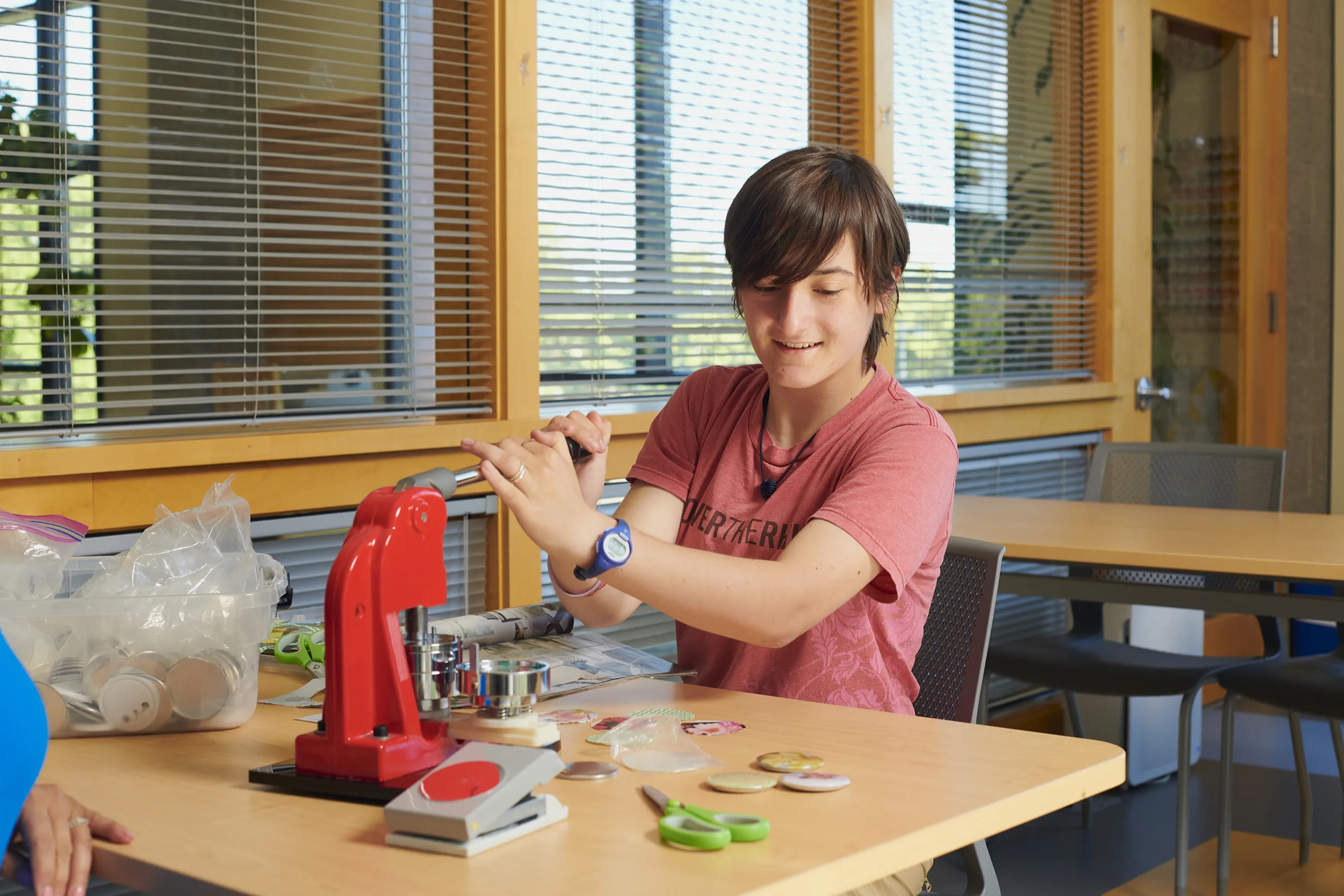 Teen boy using a button machine in library makerspace.