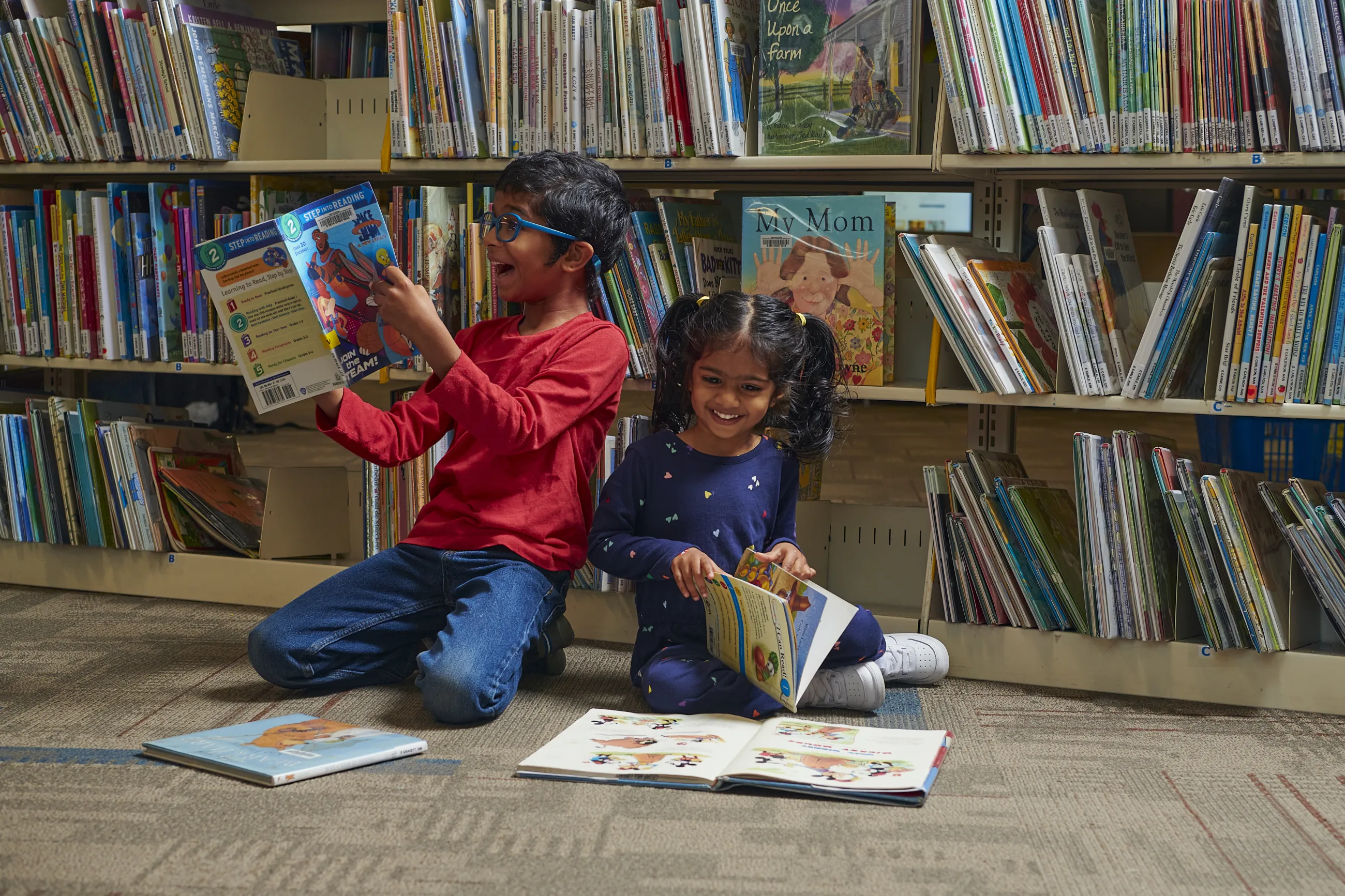 Brother and sister sitting on the floor of the library and reading picture books.