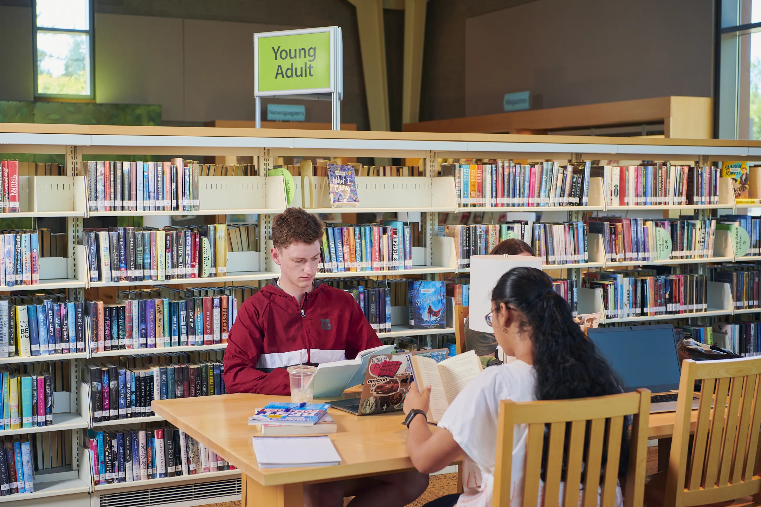 A man and and woman sitting at a desk reading books in a library.