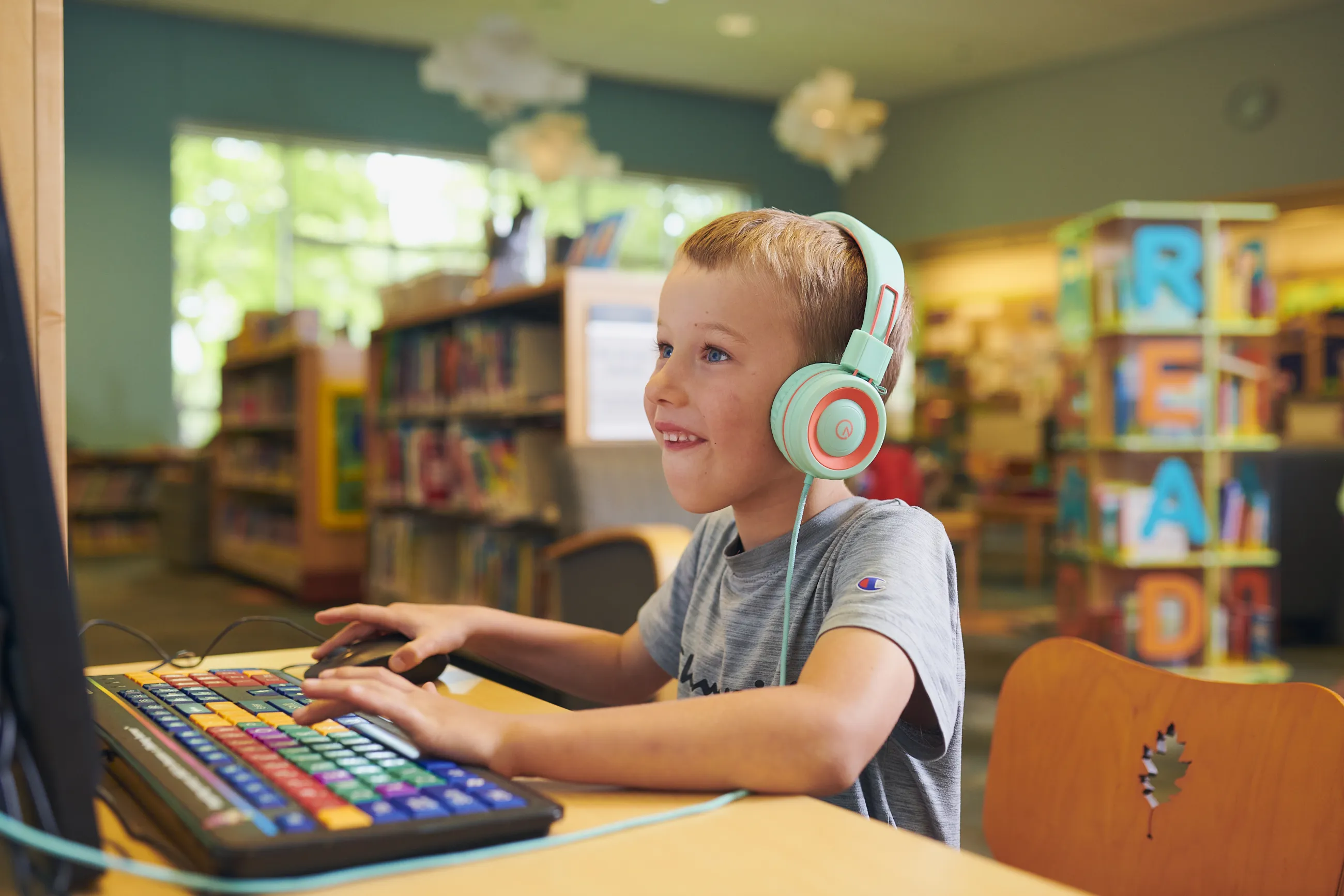 Kid with blond hair and colorful headphones smiles while pressing buttons on a keyboard