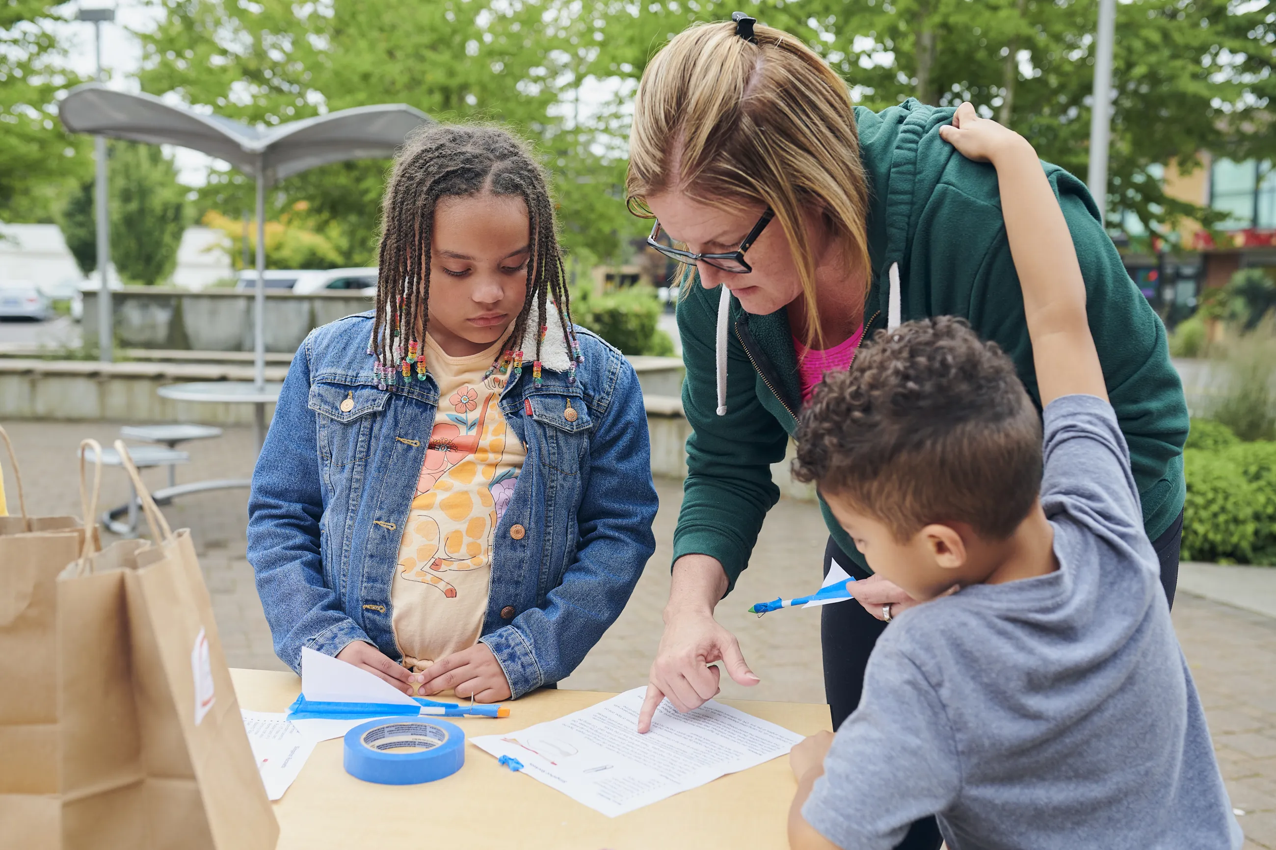 Adult and two kids reading instructions to an activity outside.