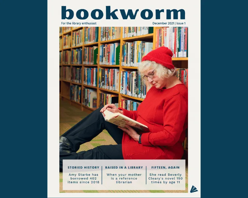 Woman wearing black pants and glasses sitting and reading against a bookshelf.