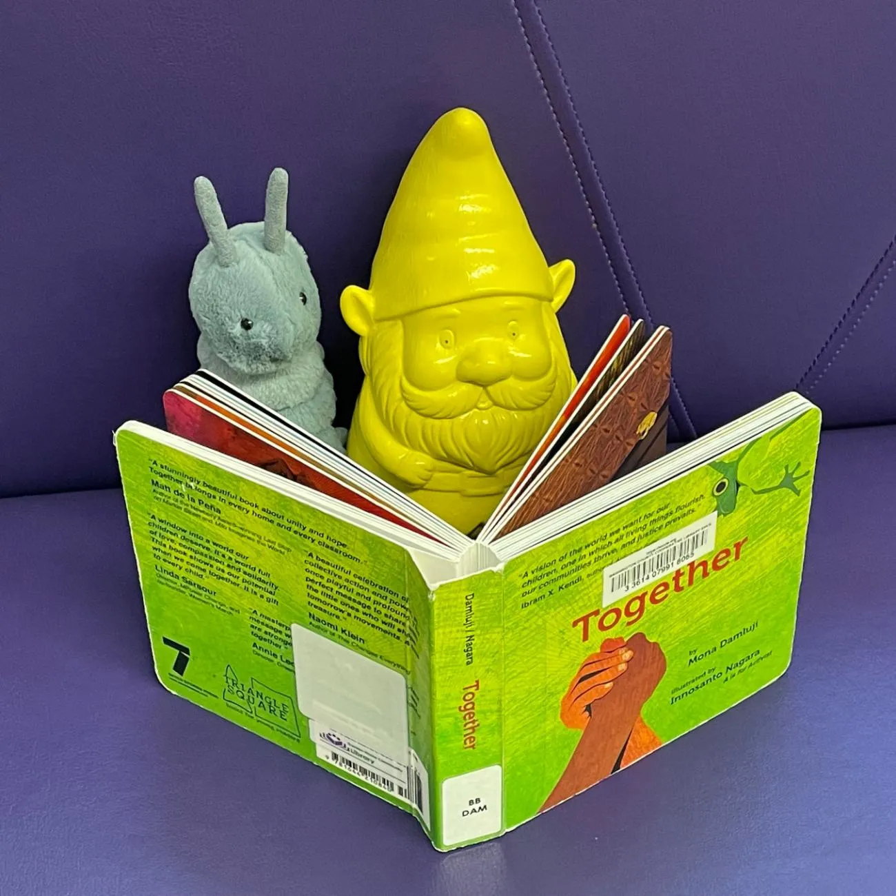 Photo of a stuffed animal caterpillar and toy gnome reading a book.