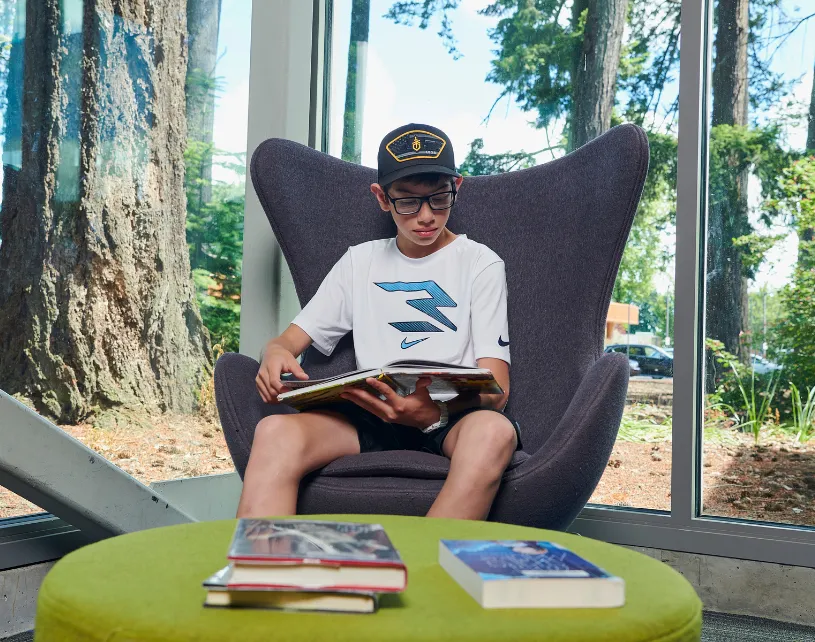 Young man reading a book in a chair at the library.