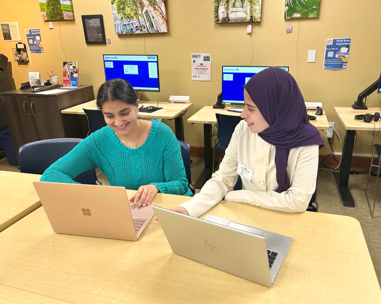 Two women sit next to each other in front of their laptops.