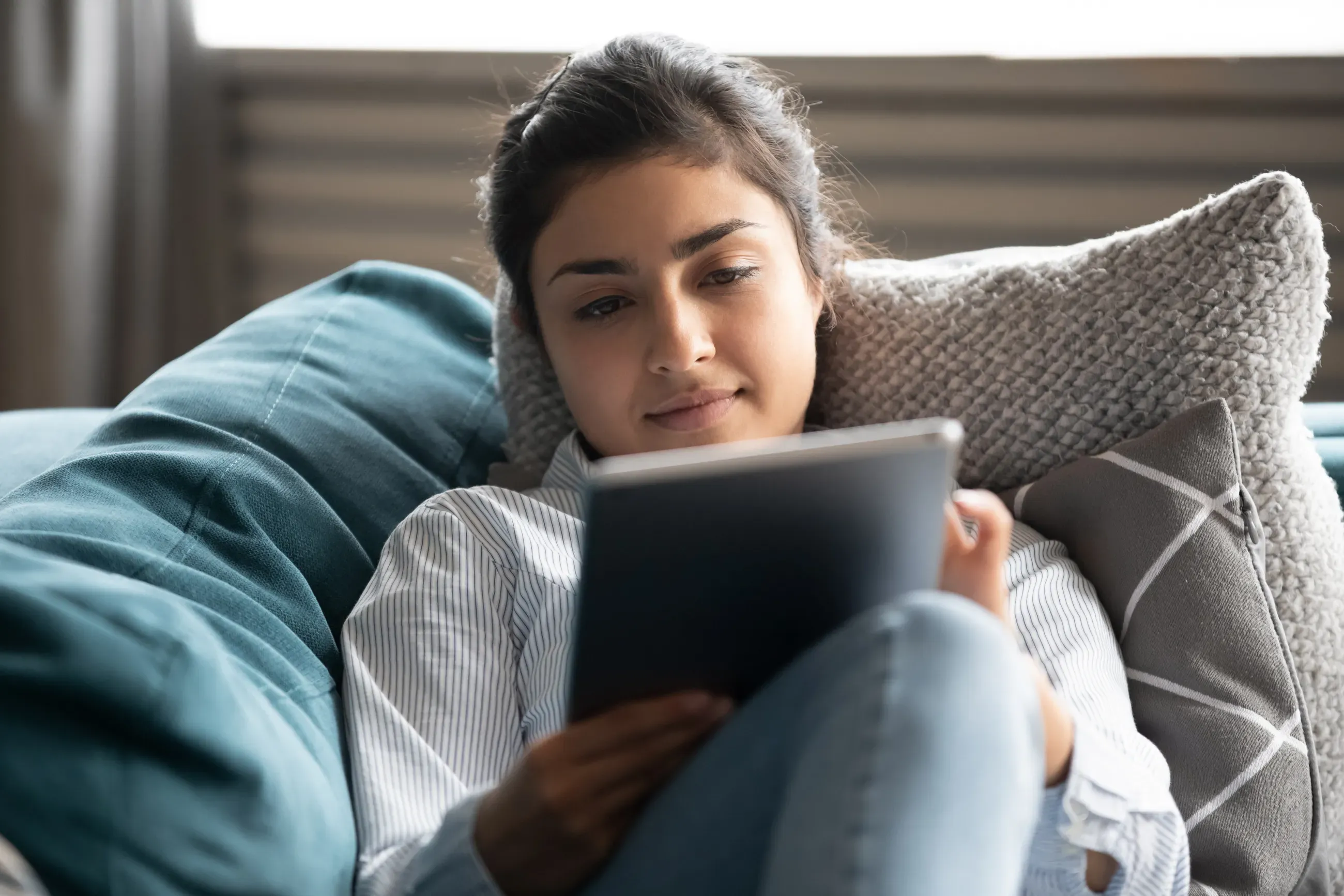 A girl on a couch looking at a tablet.