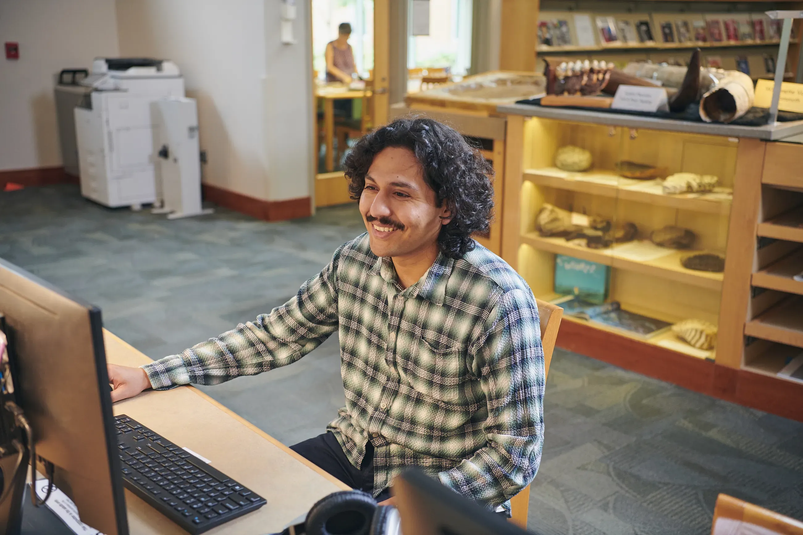 Man with dark hair sits at a computer in a library.