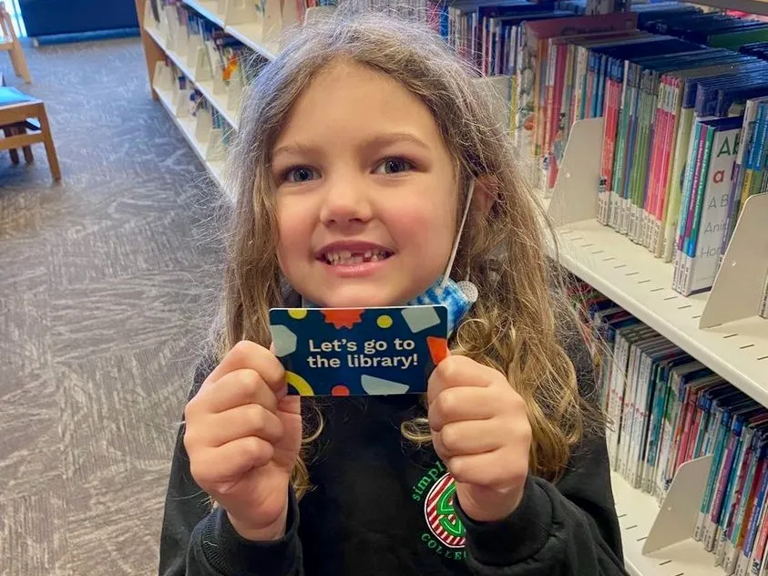 A young girl showing off her library card and smiling.