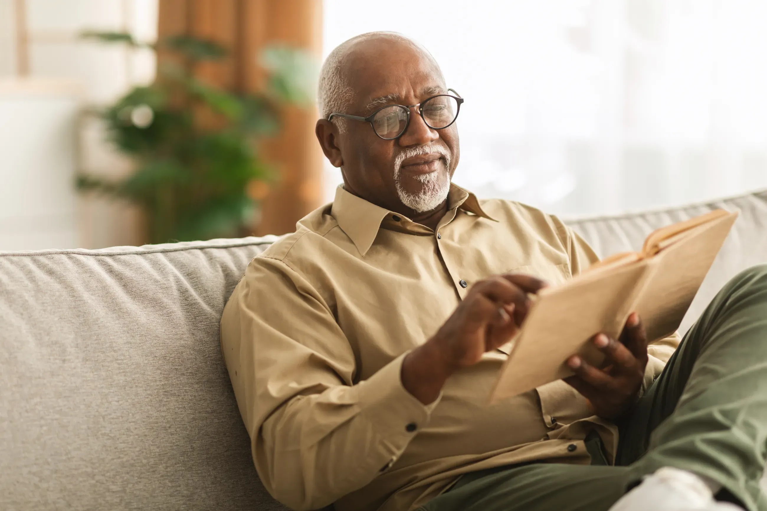 A man sits on a couch reading a book.