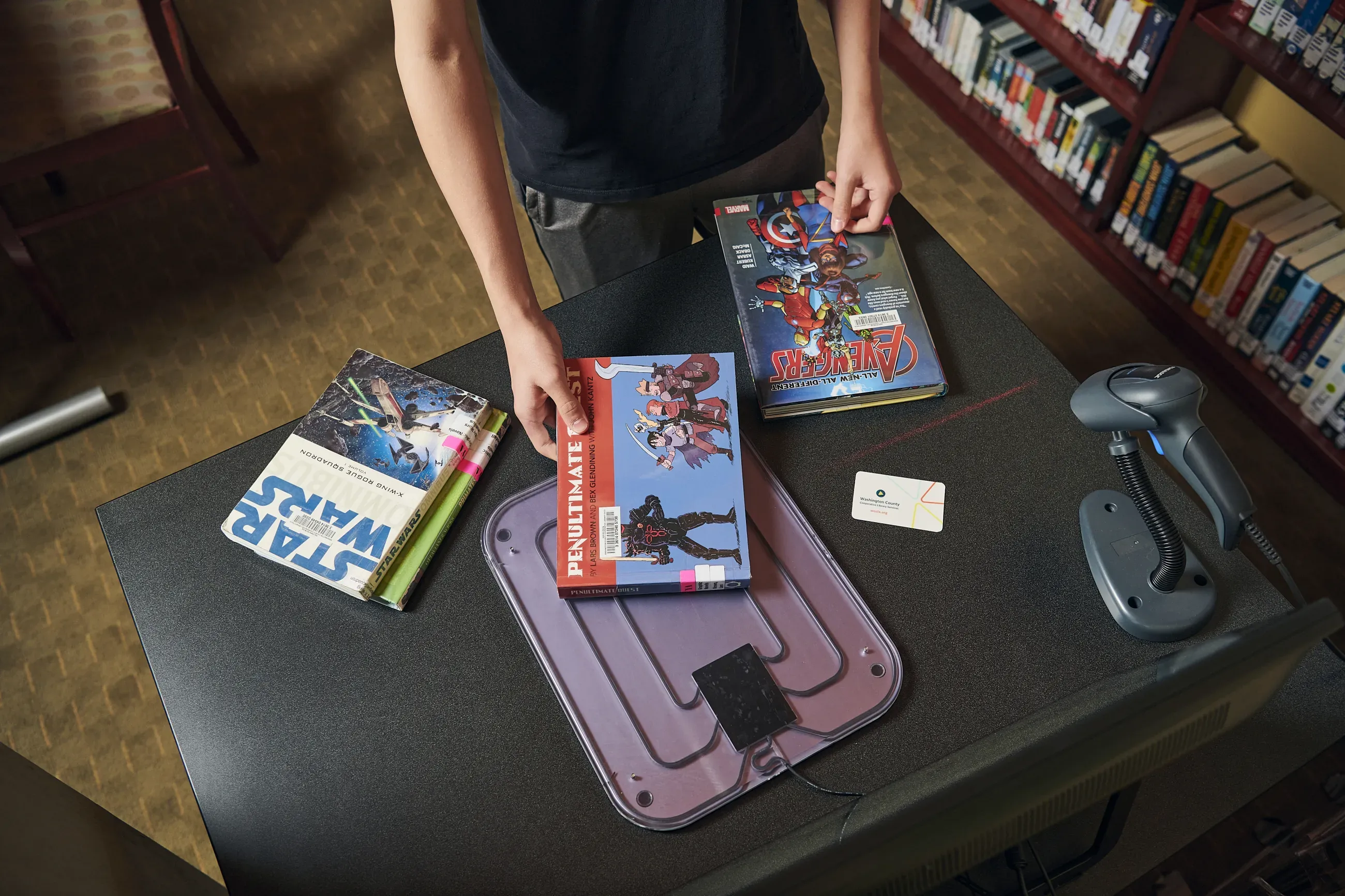 A person passes library materials over an RFID scanner.