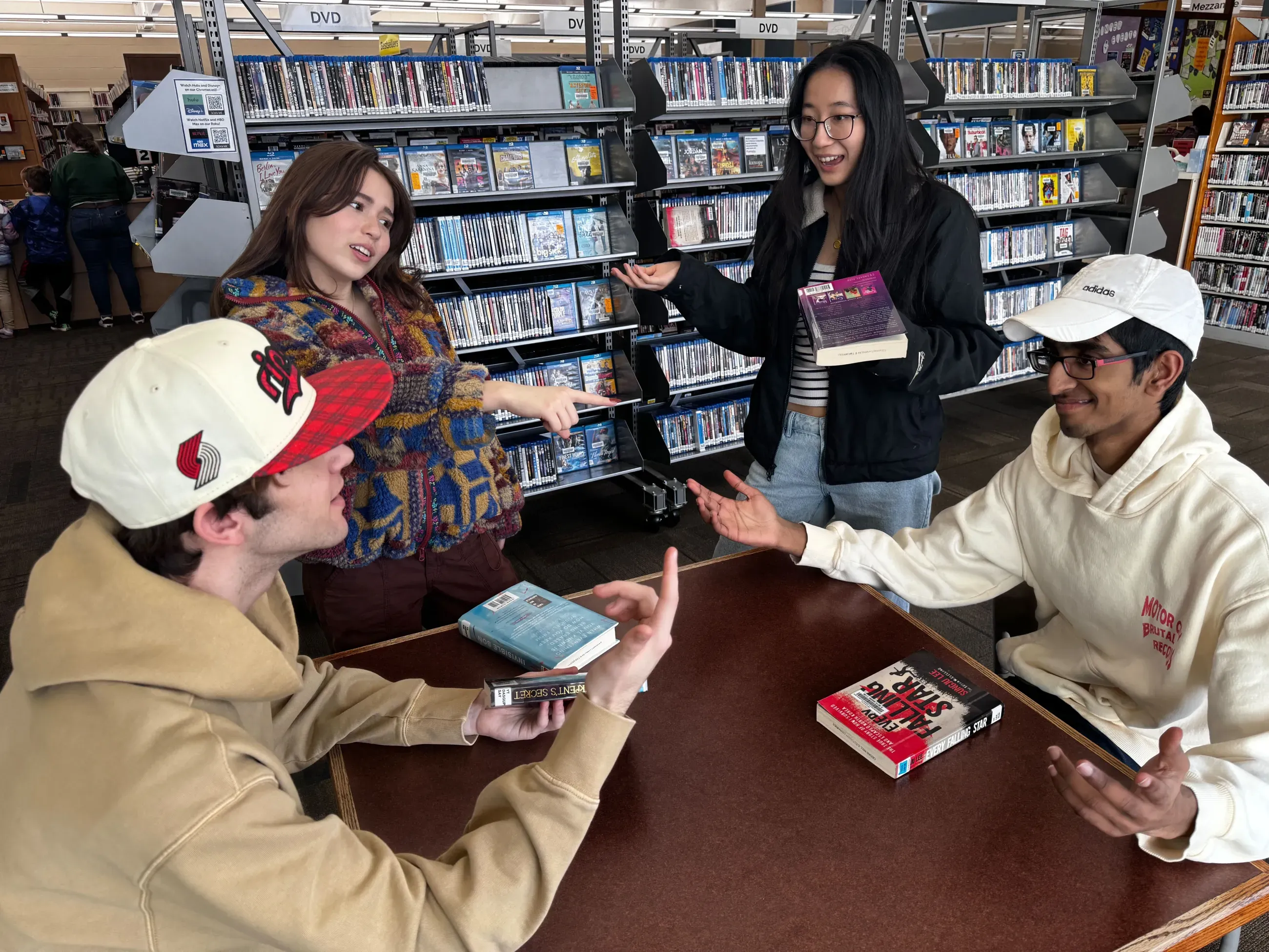 Four youths around a table, holding books and gesturing.