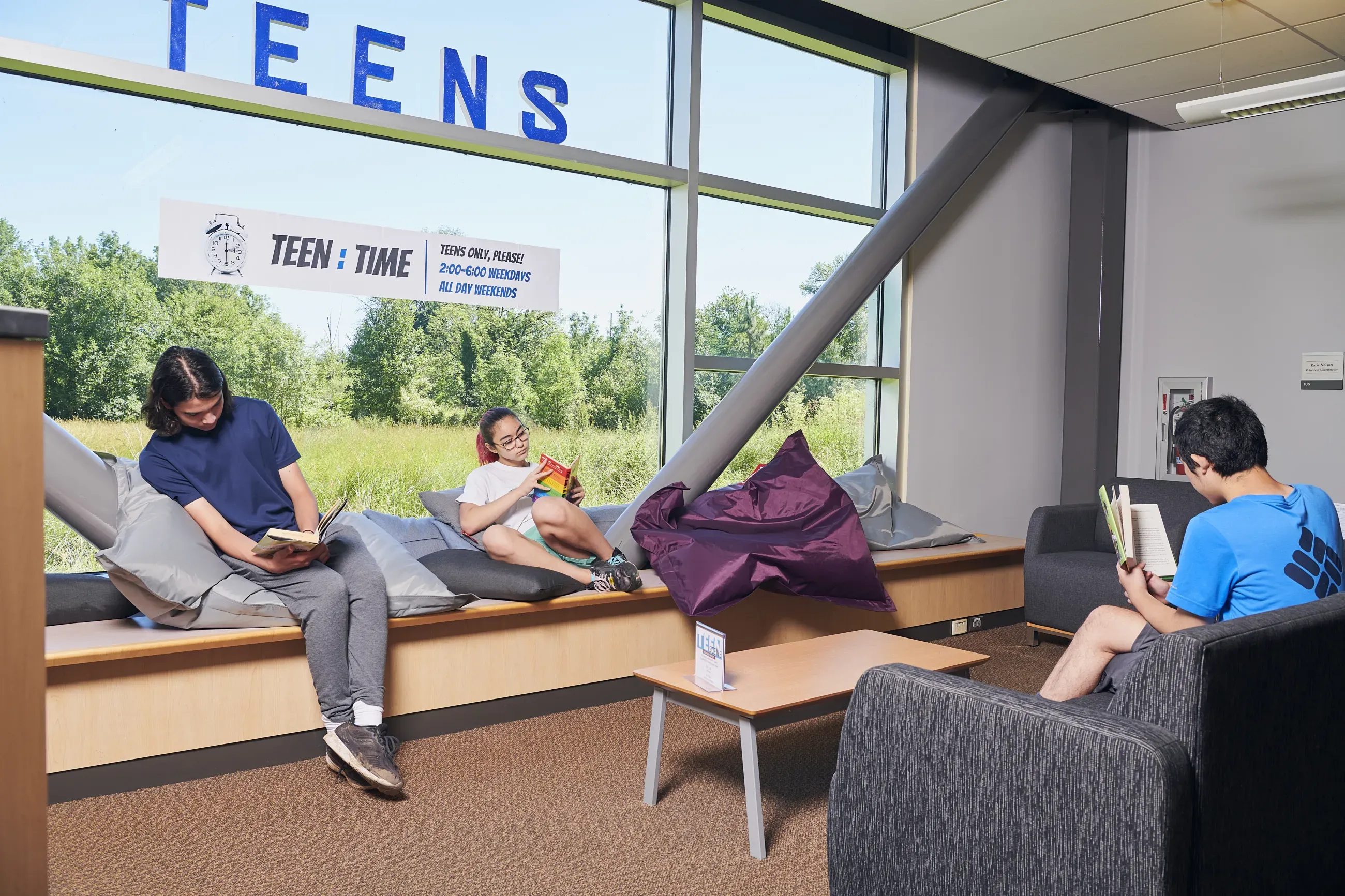 Teens reading in the Teen Room of a library, with large windows.