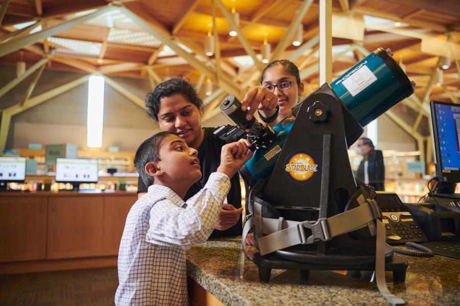 Family views a telescope on display at the library