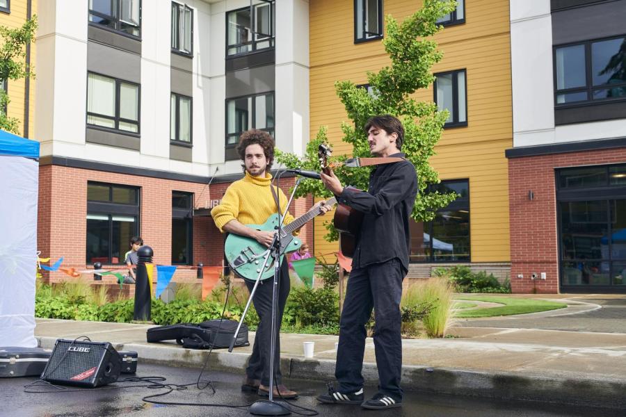 Two men playing guitar with a microphone in front of the Cornelius library