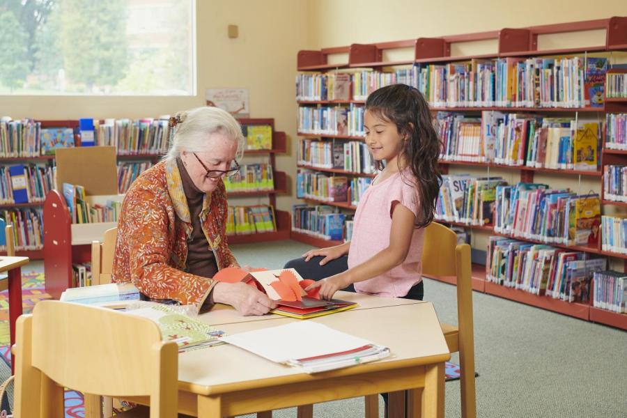 Woman and child looking at a book at a table in a library