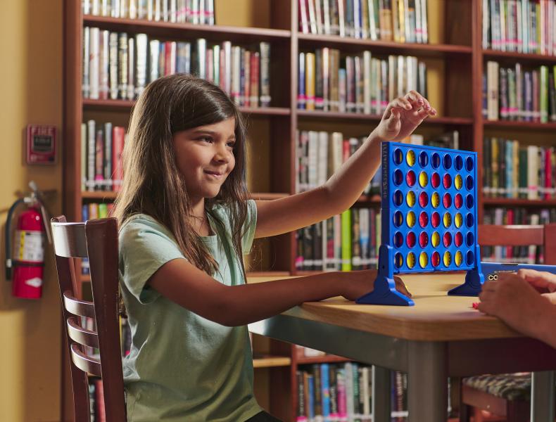 Young girl wearing green short sleeve shirt plays connect four in the library.