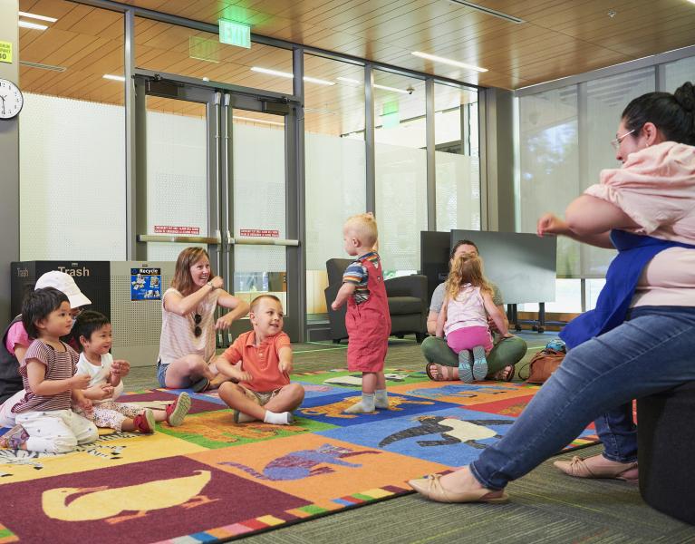 Group of toddlers and their parents smiling while listening to library staff at storytime.