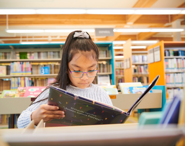 Young girl reading a book at the library.