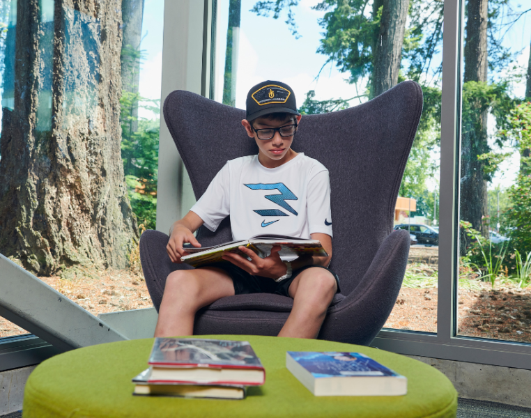 Young man reading a book in a chair at the library.