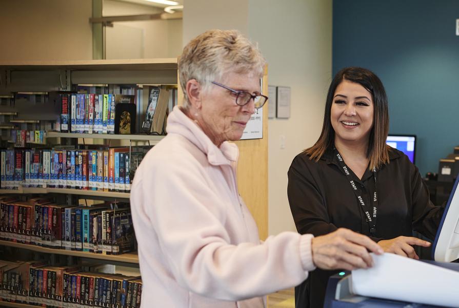 Two women standing at a copy machine in a library.